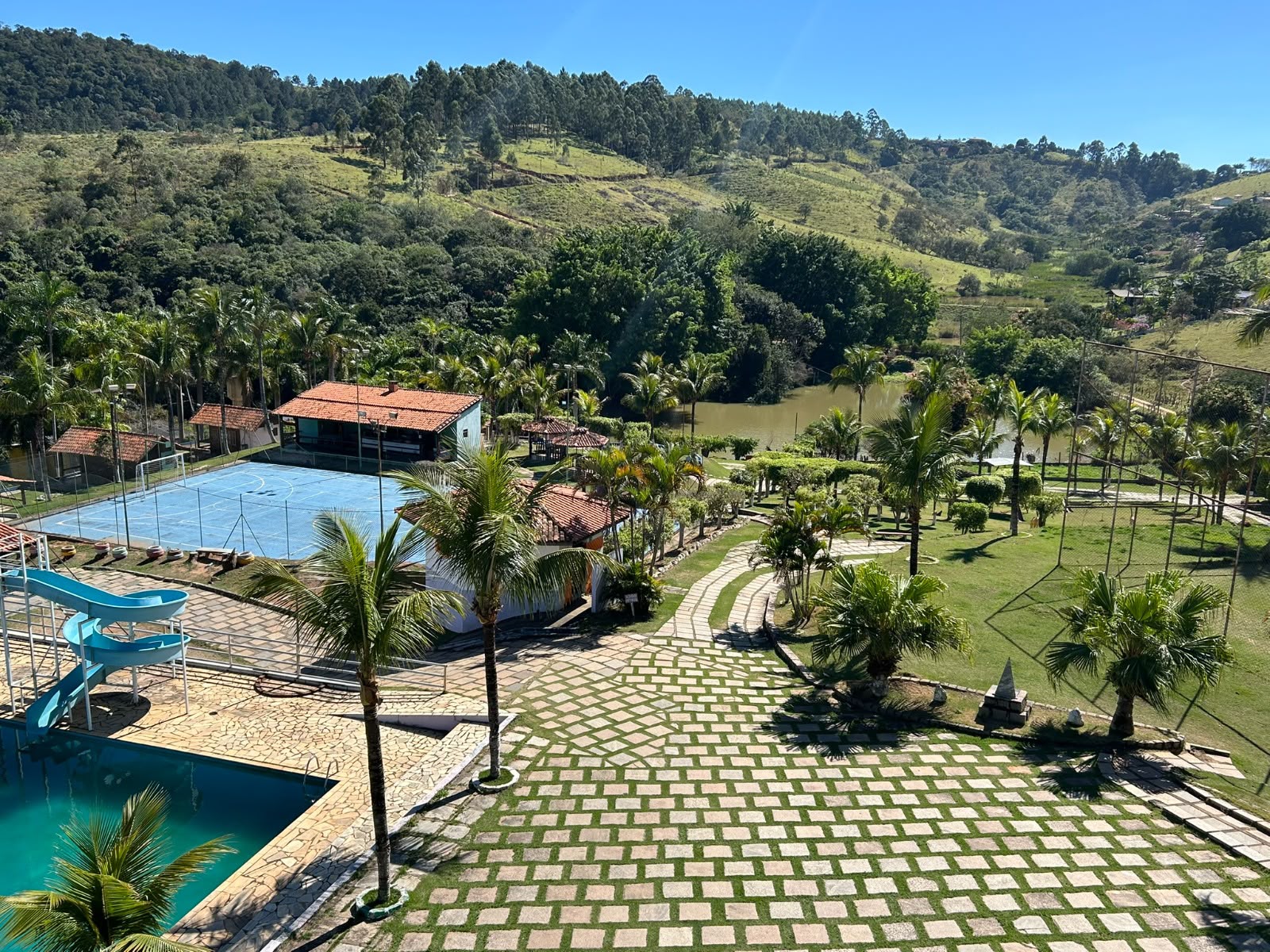 Vista real da unidade de Atibaia com jardins, piscina e quadra cercados por natureza